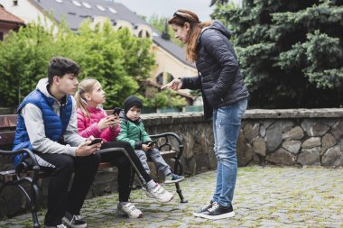Çocuklar dışarıda yürürken telefonda oynuyorlar, anneleri yakınlarda duruyor ve onlara kızıyor, telefonları kapatıp spor yapmalarını söylüyor. Cihazlara, telefonlara bağımlılık konsepti