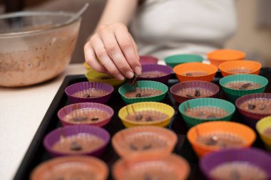 Genç bir kız en sevdiği çikolatalı kekleri evde hazırlıyor, hamuru kalıplara döküyor, çikolatayı hamurun üstüne koyuyor ve pişirecek.