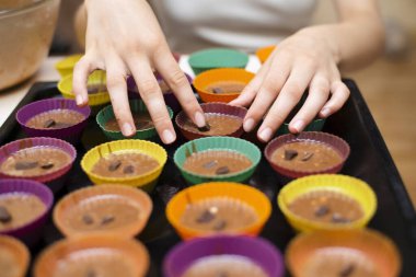 Genç bir kız yemek yapmayı öğreniyor, porsiyonlu kekleri pişirmek için özel kalıplara para döküyor, hamura çikolata koyuyor, parmaklarına odaklanıyor. Evde pasta ve tatlı yapıyorum.