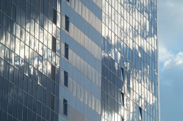 Photo of a part of the facade of a new building against a cloudy blue sky. Glass and plastic. Clouds are reflected in the facade. In light white and blue tones.