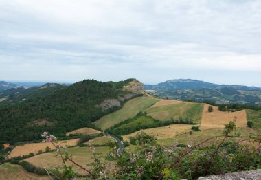 Montefeltro 'nun yumuşak, dalgalı tepeleri tarafından çerçevelenmiş kayalık uçurumuna tünemiş geniş bir San Leo manzarası.