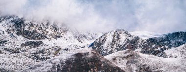 Bulutlu karlı dağ zirveleri. Panoramik kış manzarası. Doğada kış yolculuğu.