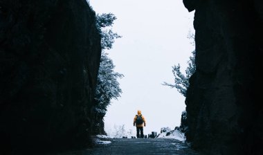 Anonymous person in a yellow jacket inside a cave. Traveler person in a winter landscape with snow. Christmas and winter holidays concept. Backpacker. clipart