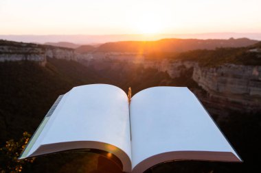 Boş sayfaları olan açık bir kitap. Güzel bir günbatımı ya da arka planda gündoğumu manzarası olan. İlhamın, eğitimin ve bilgeliğin kaynağı olarak doğaya açılma kavramı.