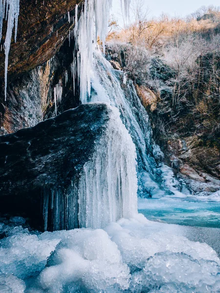 Ice formation from a frozen waterfall above a cave with white snow. Frozen waterfall. Cold and frost landscape. Tourism in Spain, Catalonia, Barcelona, Osona, Vidra, Salt del Moli. Vertical photo.