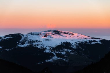 Güneşin doğuşunda ya da batışında karlı dağ zirvesi. Sakin ve rahatlatıcı doğa, dağlık doğal manzara. Gün batımında dağlarda turuncu ve ılık renkte doğa manzarası.