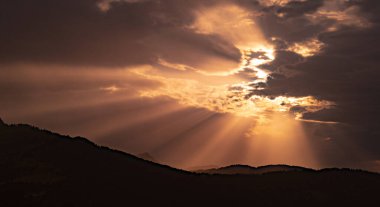 Bulutların arasından süzülen ışık ışınları güzel bir günbatımında ya da dağ siluetinin arkasında gün doğumunda. Güneş ışınları, güzel doğal turuncu ve ılık ışık ile gökyüzü manzarası.
