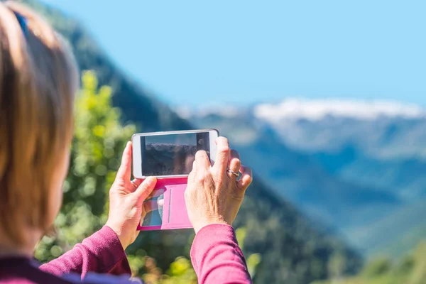 Woman taking a photo with the mobile to a mountainous landscape. Routes, excursions and mountain summer trails through nature in family. Concept of exploring and live adventures traveling in nature.