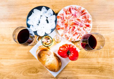 Tipik Katalan ya da İspanyol yemekleri. Domatesli ekmek, İber jambonu, bir bardak kırmızı şarap, keçi peyniri, zeytinyağı ve sarımsak. Akşam yemeği için en iyi gıda ürünleri manzarası ya da ahşap bir arka planda tapas.