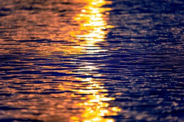 Gün batımlı deniz dalgalarının dokusu ya da gün doğumu ışığı suya yansıyor. Güneş ışınları sıcak turuncu ışıkla mavi okyanus suyunu aydınlatır. Yakından bak. Sanatsal ve yaratıcı doğa geçmişi.