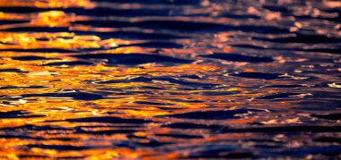 Gün batımlı deniz dalgalarının dokusu ya da gün doğumu ışığı suya yansıyor. Güneş ışınları, sıcak turuncu güneş ışığıyla mavi okyanus suyunda parlar. Sanatsal ve yaratıcı doğa geçmişi.