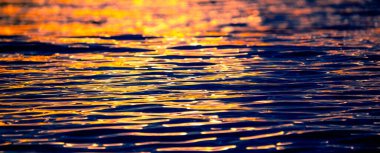 Gün batımının ışığı suya yansıyan deniz dalgaları.