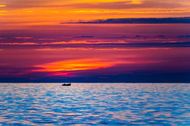 Balıkçı teknesi sabah renkli bir gündoğumuyla denizde tek başına yol alıyor. Bir balıkçı teknesi boğucu bir şekilde denizin ortasında altın sarısı bir gündoğumu ya da günbatımı renklerinde.