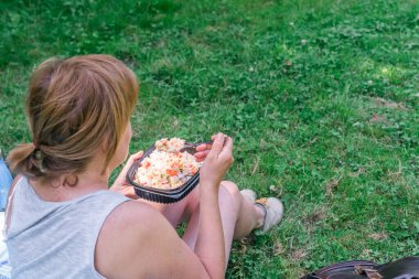 Yeniden kullanılabilir plastik bir beslenme çantasında ev yapımı yemek yiyen bir kadın. Yaz tatili, dışarıda yemek yemek..