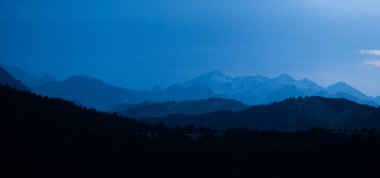Mavi saatte panoramik dağ katmanları. Alp dağlarının koyu mavi sisli siluetleri ve Pireneler 'deki köknar ağaçları ormanlarıyla manzara.