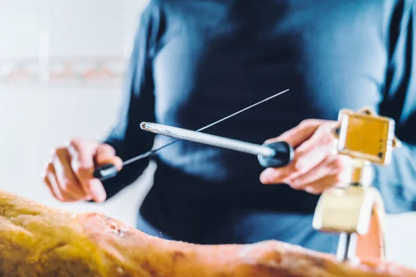 Anonymous person sharpening ham knife before cutting ham. Very well sharpened quality knife. Midsection of male chef\'s sharp knife in the kitchen.