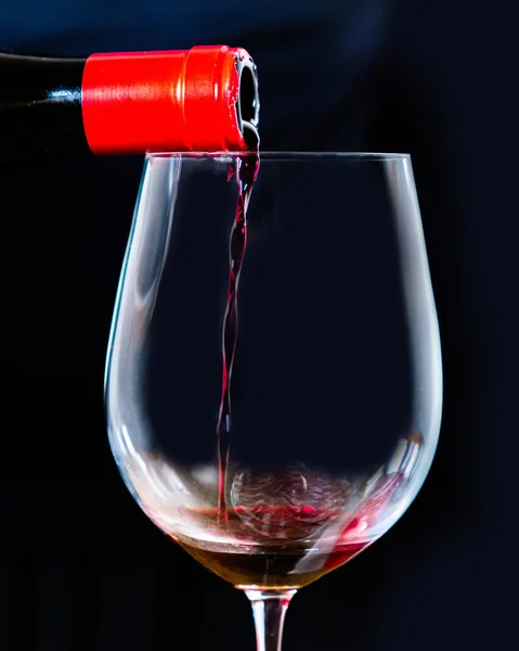 Sommelier serving Spanish black wine in an elegant crystal goblet with a black background. Pouring red wine from bottle into the wineglass on black.