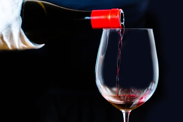 Sommelier serving Spanish black wine in an elegant crystal goblet with a black background. Pouring red wine from bottle into the wineglass on black.