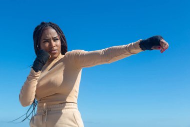 Genç afro siyah kız dövüş sanatları eğitimi alıyor, açık havada deniz ve mavi gökyüzü geçmişiyle boks yapıyor. Tavır, spor, egzersiz.