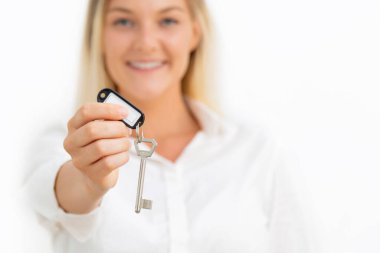 Genç ve güzel bir kadın, dairenin anahtarlarını beyaza gösteriyor. Emlak kavramı.
