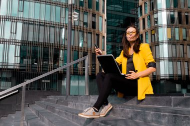 Dizüstü bilgisayarlı serbest çalışan iş merkezinin yanındaki merdivenlerde oturuyor.,