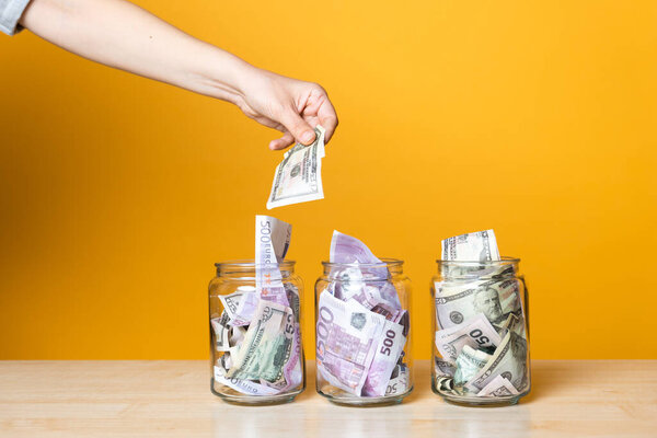 Мультивалютные счета, концепция. Доллары и евро в стеклянной банке на ярком желтом фоне.