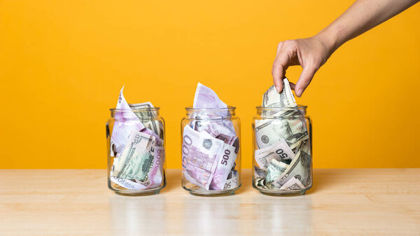Мультивалютные счета, концепция. Доллары и евро в стеклянной банке на ярком желтом фоне.