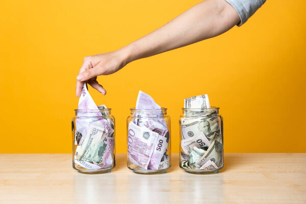 Мультивалютные счета, концепция. Доллары и евро в стеклянной банке на ярком желтом фоне.