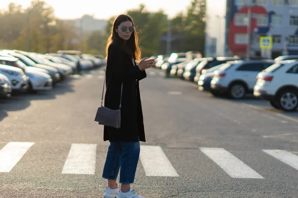 Auto delen, een jonge vrouw met een mobiele telefoon in haar hand in de buurt van de parkeerplaats. — Stockfoto