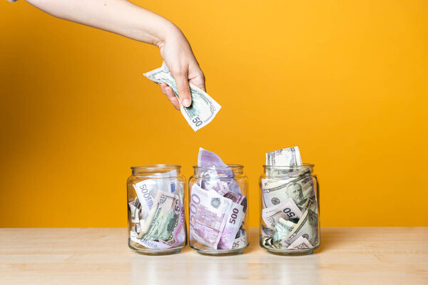 Мультивалютные счета, концепция. Доллары и евро в стеклянной банке на ярком желтом фоне