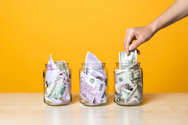 Мультивалютные счета, концепция. Доллары и евро в стеклянной банке на ярком желтом фоне
