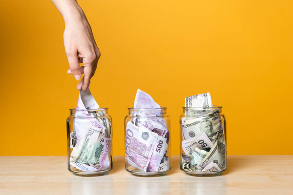 Мультивалютные счета, концепция. Доллары и евро в стеклянной банке на ярком желтом фоне.