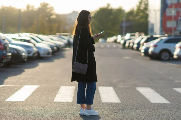 Autómegosztás, egy fiatal nő mobiltelefonnal a kezében a parkolóban.. — Stock Fotó