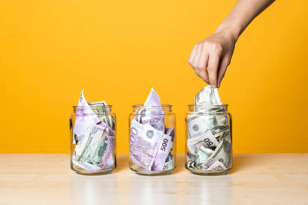 Мультивалютные счета, концепция. Доллары и евро в стеклянной банке на ярком желтом фоне