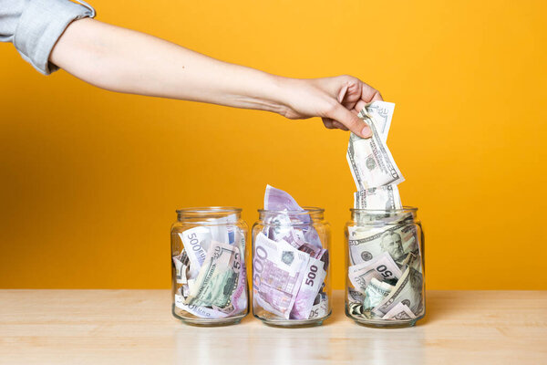 Мультивалютные счета, концепция. Доллары и евро в стеклянной банке на ярком желтом фоне.