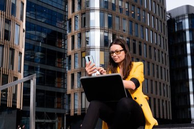 Dizüstü bilgisayarlı serbest çalışan iş merkezinin yanındaki merdivenlerde oturuyor.,