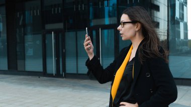 Paltolu ve gözlüklü genç bir kadın akıllı telefon kullanıyor.,