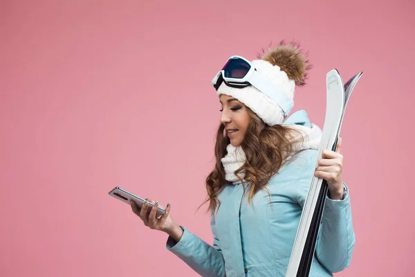 Молода жінка з лижами використовує смартфон для планування катання на лижах. Зимові канікули на гірськолижному курорті — стокове фото