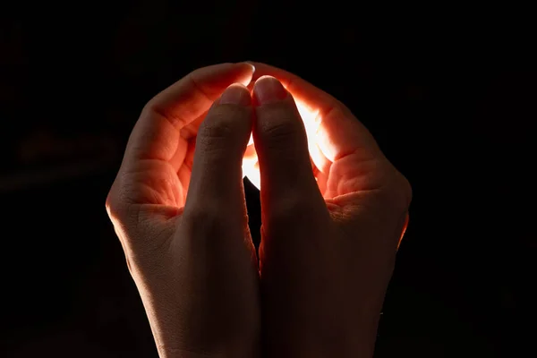 Duas mãos dobradas apertar a luz dentro, luz avermelhada dentro das mãos, fundo preto. — Fotografia de Stock