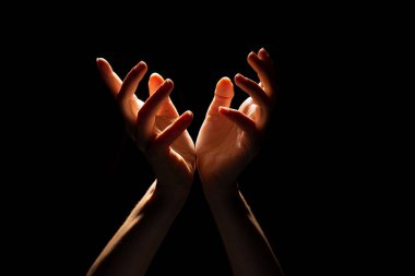 Üzerinde ışık olan katlanmış güzel eller, siyah arkaplan. Dua etmek ya da bir mucize yaratmak.