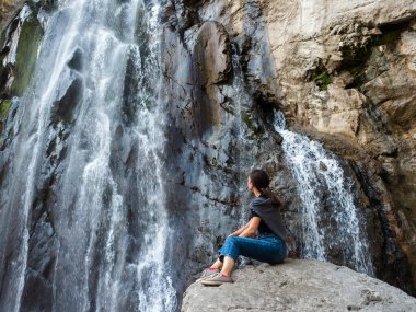 Ormanda turizm, dağ şelalesinin arka planında genç bir kadın.,