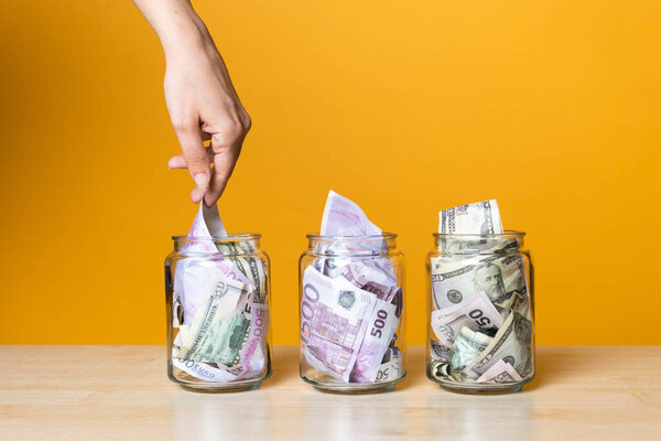 Мультивалютные счета, концепция. Доллары и евро в стеклянной банке на ярком желтом фоне