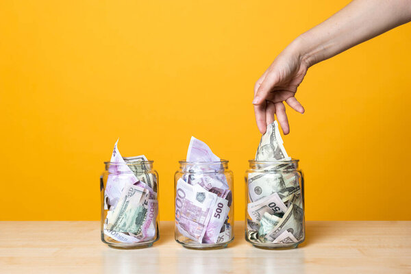 Мультивалютные счета, концепция. Доллары и евро в стеклянной банке на ярком желтом фоне.
