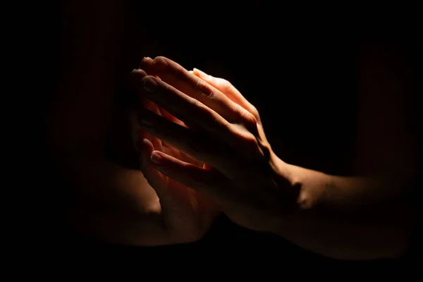 Praying hands on a black background. Light from above. Hands folded in prayer.