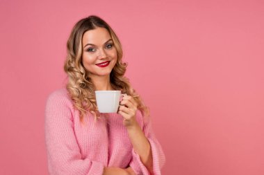 Kahve iç, sıcak bir içeceğin tadını çıkar. Sıcak pembe kazaklı genç bir kadın.