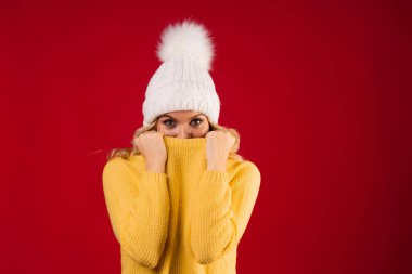 Sarı örgü süveterli, kırmızı arka planda tatlı ve gülümseyen sarışın kadın.,