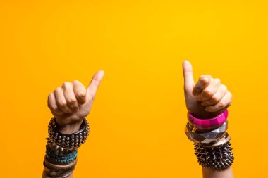 El hareketleriyle. Baş parmaklar yukarı, onay gibi. Bir sürü bileziği olan iki kadın eli, gençlerin eğlence tarzı..
