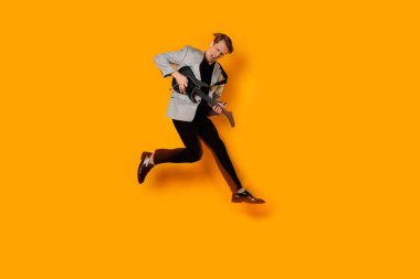 Adam gitar solosu yapıyormuş gibi yapıyor, genç ve şık bir adam oyuncak gitarıyla zıplıyor ve eğleniyor..