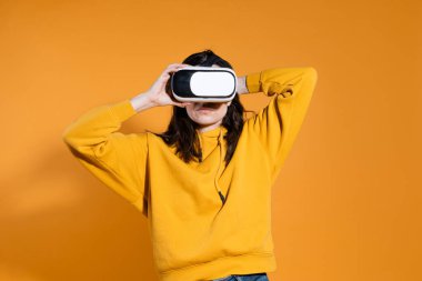 Sarı arka planda sanal gerçeklik cihazı olan genç bir kadın..