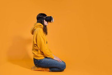 Sarı arka planda sanal gerçeklik cihazı olan genç bir kadın..